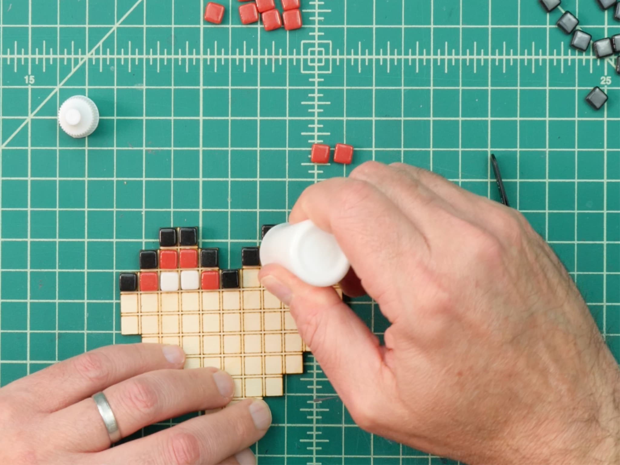 Hands placing small mosaic tiles onto a grid.